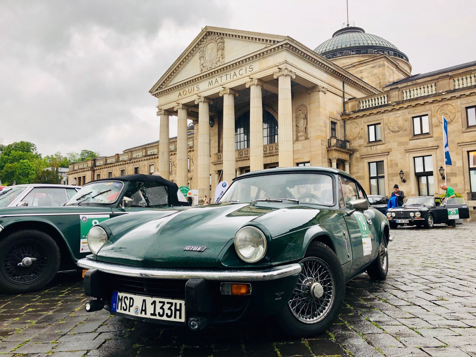 Triumph GT6 mit Startnummer vor dem Kurhaus Wiesbaden, dahinter weitere Rallyefahrzeuge